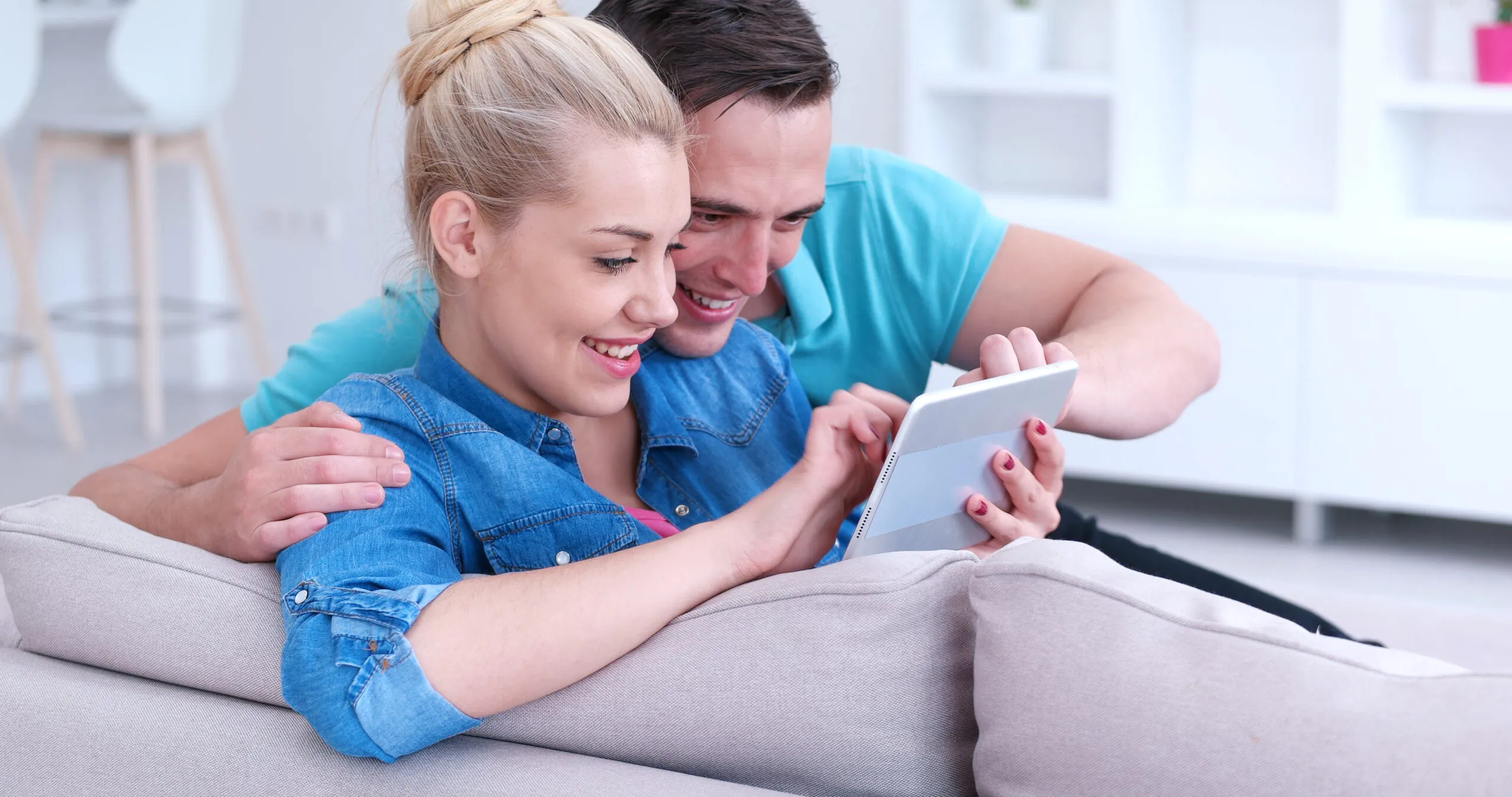 Young couple relaxing at luxurious home with tablet computers reading in the living room on the sofa couch.